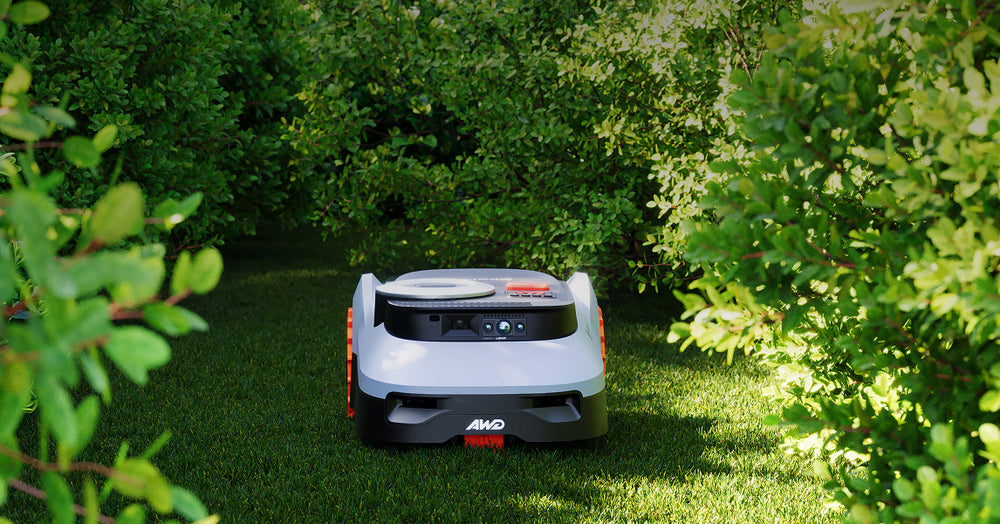 Navimow i110N robot lawn mower mows grass between green bushes.
