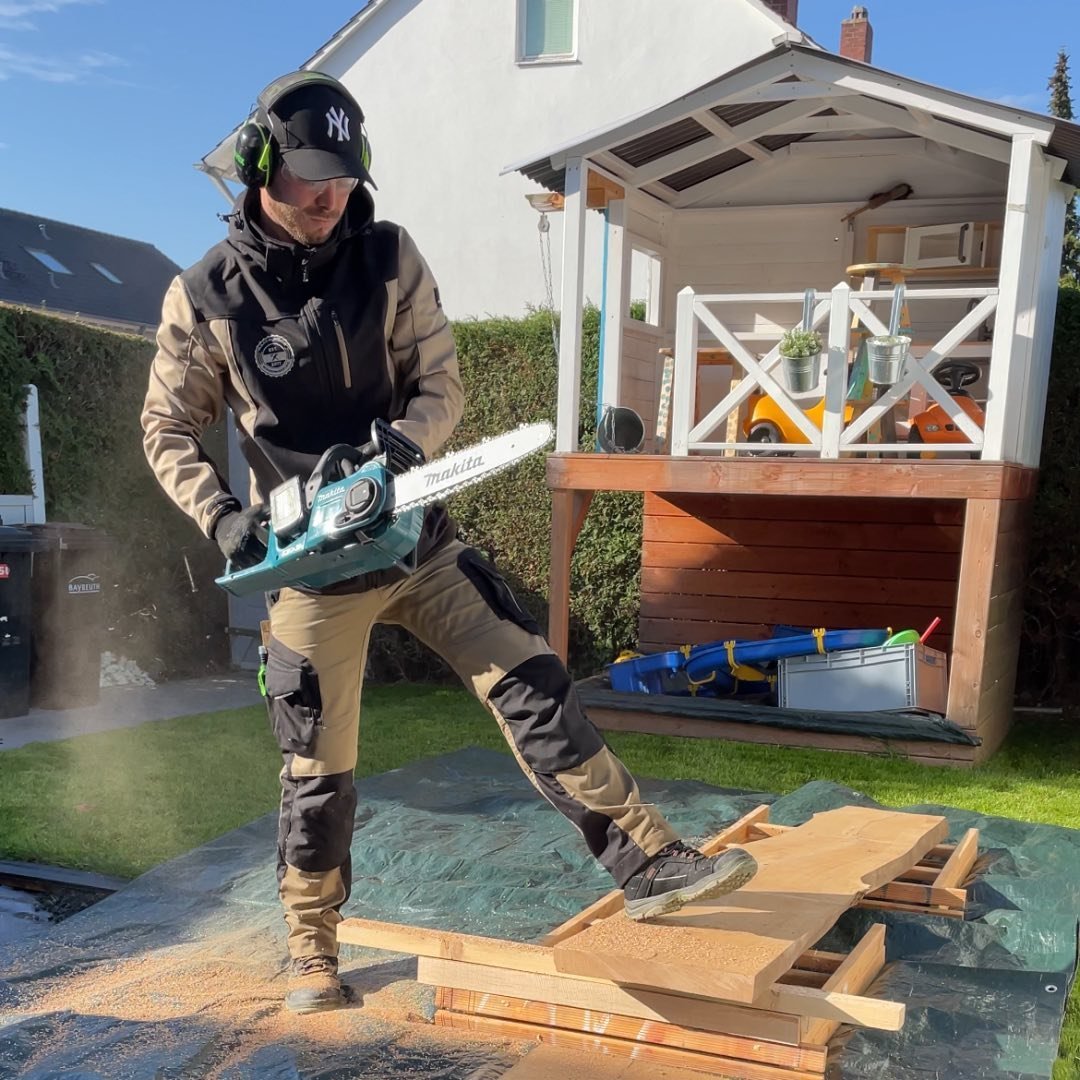 Man uses a Makita chainsaw to cut wood in garden.