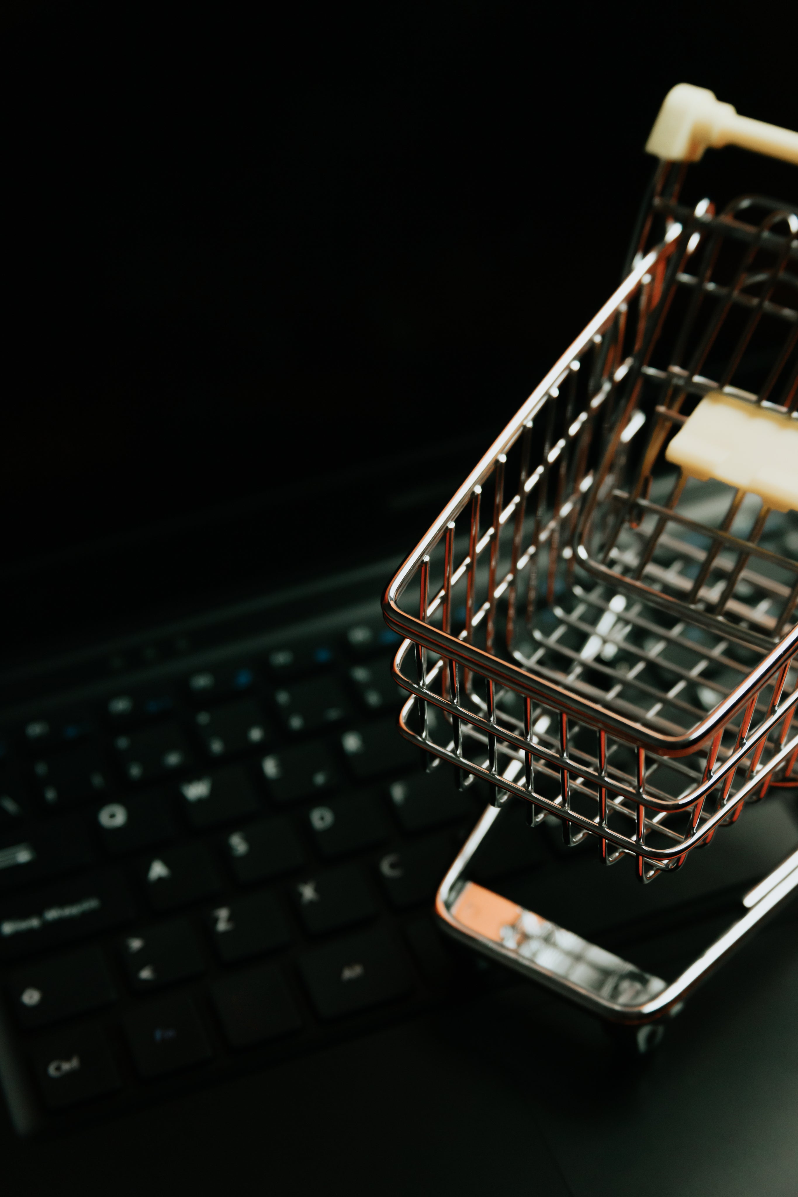 Small metal shopping cart sits on a black laptop keyboard.